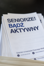 Zbliżenie na nagłówek ulotki z wyraźnym, ciemnoniebieskim napisem „SENIORZE! BĄDŹ AKTYWNY” wydanej przez Gdański Uniwersytet Trzeciego Wieku.